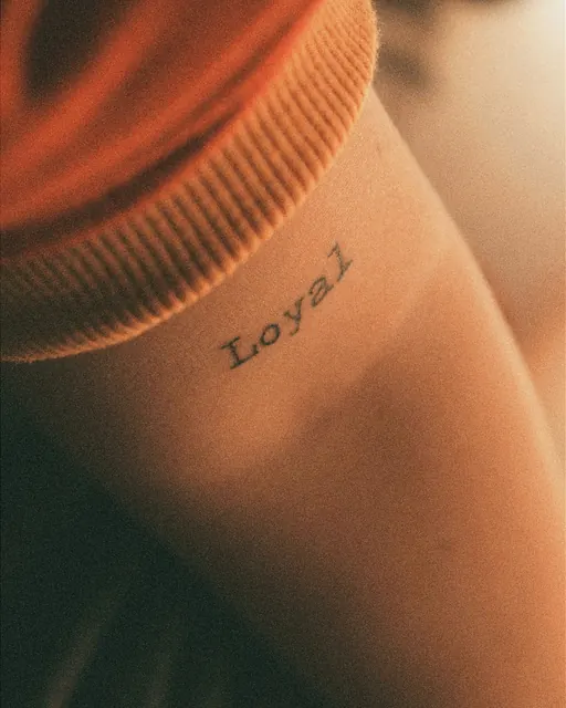Small typewriter-font lettering tattoo reading Loyal, healed