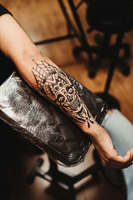 Blackwork skull and spiderweb tattoo on an inner forearm, fresh