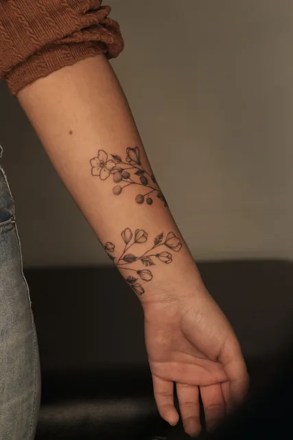 Fine line blossom and berry vine tattoo wrapping the forearm, healed