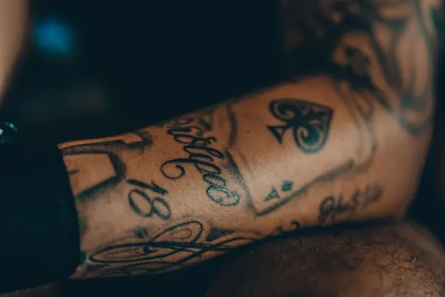 Script lettering and playing card tattoos on a forearm, healed