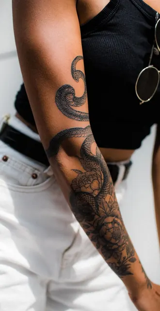 Blackwork snake and peony wrapping the forearm and upper arm, healed