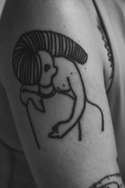 Bold blackwork illustrative tattoo on an upper arm, healed